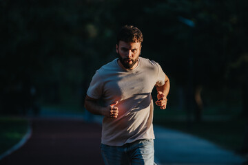 A focused man runs on a dimly lit path, showcasing determination and fitness.
