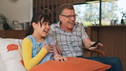 Grandfather and granddaughter together watch interesting entertainment media on TV. Old senior use...
