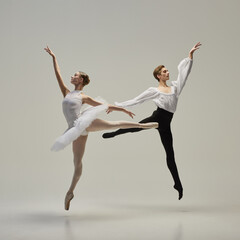 Two ballet dancers leaping in perfect synchronization, arms reaching, bodies forming clear lines against white studio background. Concept of classic dance, freedom, dynamic energy, synergy.