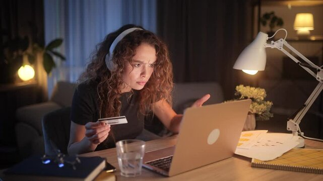 Frustrated young woman trying to make an online purchase at night. She enters her card details, but the payment fails, making her angry and annoyed while looking at her laptop screen