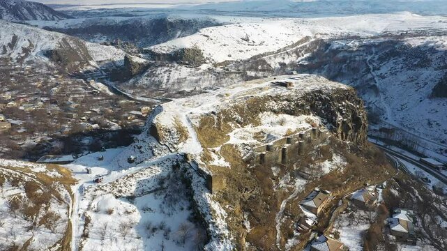 Aerial 4K drone video of a winter view of Bjni village in Kotayk, Armenia, featuring the historic Bjni Fortress, surrounded by snow-covered village houses, winding streets, and the Hrazdan River