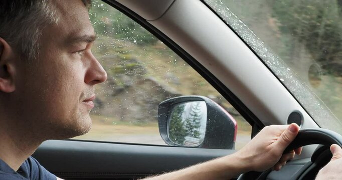 Focused driver navigating car through rainy conditions, maintaining firm grip on steering wheel while maintaining steady gaze ahead, embodying calm concentration during challenging weather journey