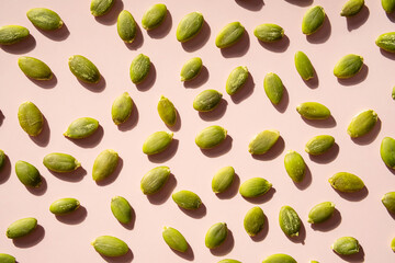 Peeled pumpkin seeds on pink surface.