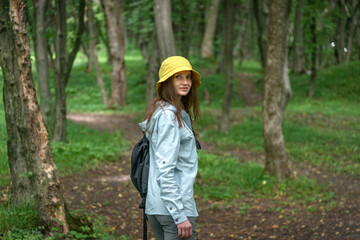 Female hiker with a backpack walks through sunlit forest in the mountains, surrounded by lush green...