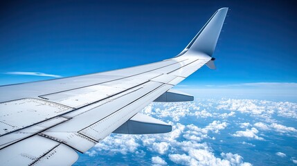 Obraz premium A close-up of an aircraft wing cutting through the clear sky, with the faint outline of distant land visible beneath the clouds.