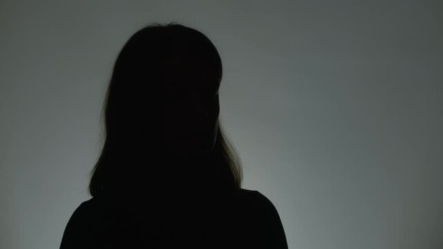 Anonymous interview with a woman who suffered from violence. Female silhouette. Hidden person speaking in a dark studio.