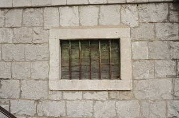 Window with metal bars. Traditional Croatian house facade. White stones wall.