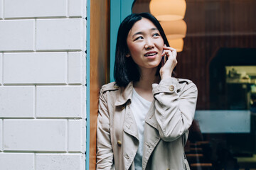 Calm modern Asian woman speaking on smartphone on street