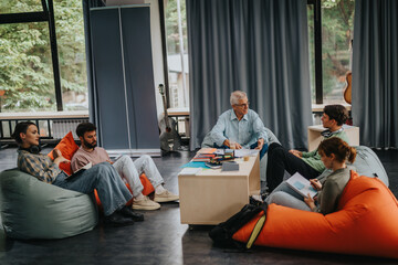 A professor interacts with students in a casual classroom environment. They are seated on bean bags, fostering a creative and open learning atmosphere.