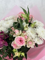 Bouquet with pink roses, eustoma and white chrysanthemums. Pink wrapping paper. Vertical