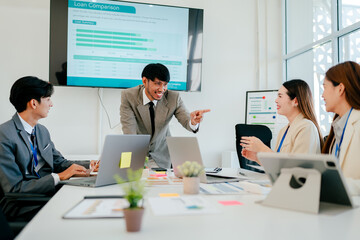 Group of people are sitting around a table with a large screen behind them
