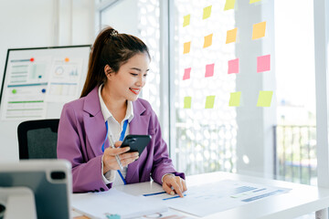 Woman in a purple jacket is sitting at a desk with a cell phone in her hand