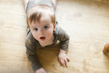 Naklejka premium Adorable baby on wooden floor. Happy cute infant portrait on floor learning to crawl, space for text. Child development and childcare