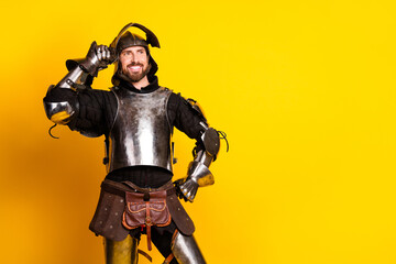 Young man in medieval knight armor posing with cheerful expression on bright yellow background
