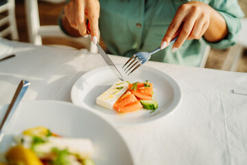 Front view of woman's hand eat greek salad on the table in restaurant


