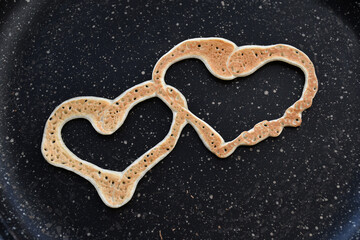 A pancake in the form of two joined hearts on a black spotted pan. selective focus. Maslenitsa holiday. curly pancakes