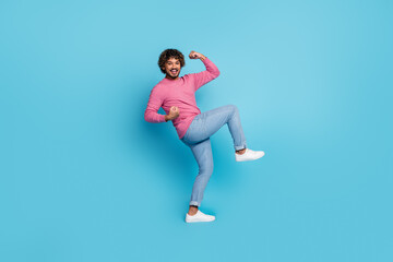 Happy stylish young man wearing pink pullover and denim jeans playfully posing on a blue background with a cheerful expression