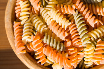 colorful fusilli pasta in a wooden bowl on the table, top view