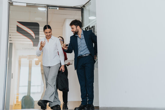 A group of business colleagues leaving an office building share a lively conversation, exemplifying teamwork and collaboration in a modern work environment.