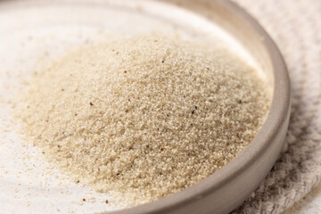 Raw uncooked fonio seeds on a plate on white table, top view. African ancient pseudocereal