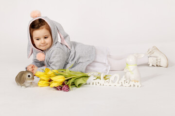 Cute Toddler in Bunny Costume Lying Next to Easter Decorations and Yellow Tulips
