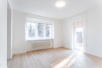 Fototapeta premium Empty living room with balcony door and white walls illuminating by sunlight