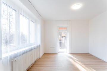 Empty living room with balcony door and large windows illuminating modern apartment