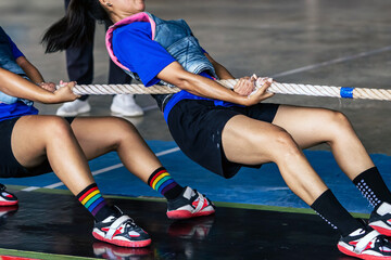 Female students participate in tug of war match. Young woman playing active games pulling rope in high school. Joyful girls playing tug of war games. Team player battle tug match for pull game.