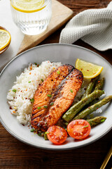 Baked salmon fish steak with asparagus fried rice and lemon slice. Delicious lunch or dinner for every day. Wooden background
