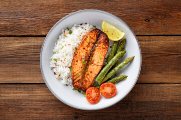 Baked salmon fish steak with asparagus fried rice and lemon slice. Delicious lunch or dinner for every day. Wooden background, top view