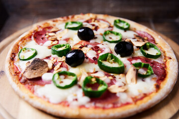 Pizza with salami and mozzarella cheese, jalapeno pepper and black olives. Wooden background. Soft focus. Close up.