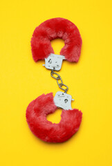 Red sexy fluffy handcuffs on a yellow