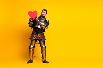 Fototapeta premium Young armored man holding a heart on bright yellow background exuding novelty and charm