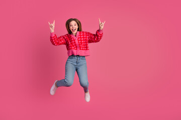 Excited young woman in vibrant pink cardigan expresses joy and energy against a bright pink background while jumping mid-air