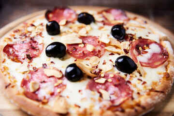 Pizza with salami and mozzarella cheese. Wooden background. Soft focus. Close up.