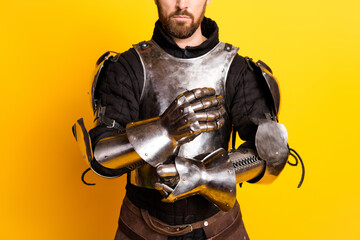Medieval knight in shining armor posing against bright yellow background, showcasing traditional historical costume