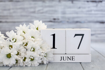 White wood calendar blocks with the date June 17th and white daisies. Selective focus with blurred background. 