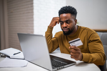 Young African-American businessman using laptop for online banking, holding his credit card and...