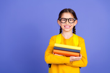 Smiling young girl in casual yellow outfit holding colorful books against a vibrant purple...