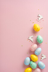 Brightly vertical colored Easter eggs laid out on a pink surface with small wooden bunnies in...