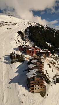 drone video of French luxury ski resort Courchevel in European Alps with ski slope and people skiing at it with wooden mountain hotels nearby  