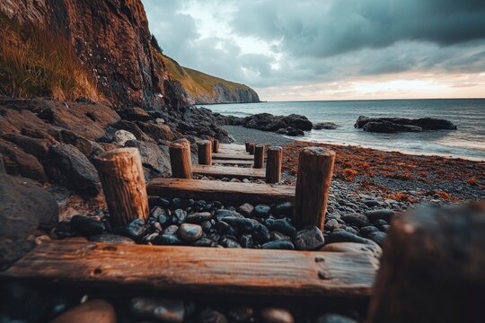 Scenic view of wooden steps leading to a rocky beach under a dramatic cloudy sky at sunset