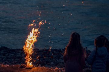Sea night breeze and flame. Friendly evening by the fire. People or kids girls sitting around a campfire. burns with bright sparks brightly, illuminating them and the surrounding landscape, warm light