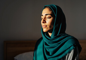 Serene muslim woman wearing a hijab praying with closed eyes, embracing the spiritual atmosphere of ramadan