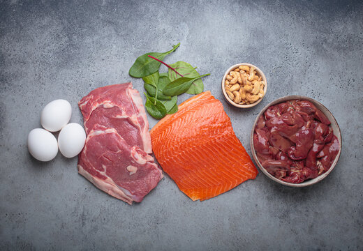 Fresh salmon fillet, raw beef, nutritious eggs, spinach, nuts cashews and liver arranged on a gray background, iron rich foods essential for a balanced diet concept