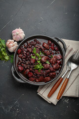 Feijoada, a traditional brazilian stew in a cast iron pot, accompanied by fresh garlic and parsley,...