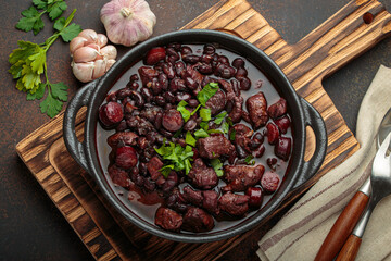 Brazilian feijoada, a hearty stew of black beans, various cuts of meat, and sausage, garnished with fresh parsley, in a rustic cast iron pot, ready to be served