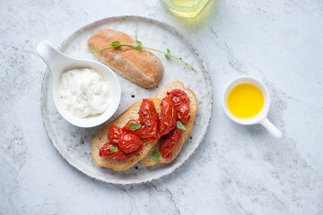 Plate with stracciatella cheese and roasted tomato bruschettas on a white stone background, horizontal shot, view from above