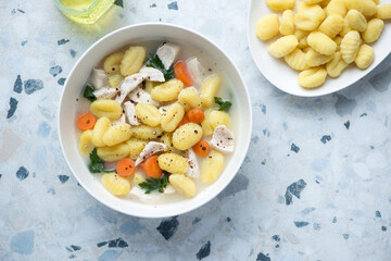Bowl of chicken soup with potato gnocchi, horizontal shot on a white and blue granite background with space, view from above