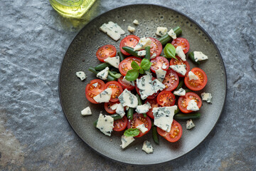Plate with cherry tomato, green beans and blue cheese salad, horizontal shot on a dark-grey granite background, elevated view